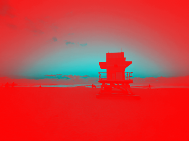 An image of the backside of lifeguard tower on the beach, facing the ocean, styleized with red overlay in foreground. There is blue sky and ocean in the distance.